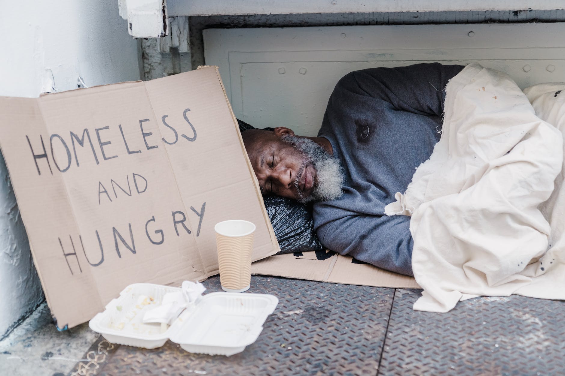 photo of a homeless man sleeping near a cardboard sign