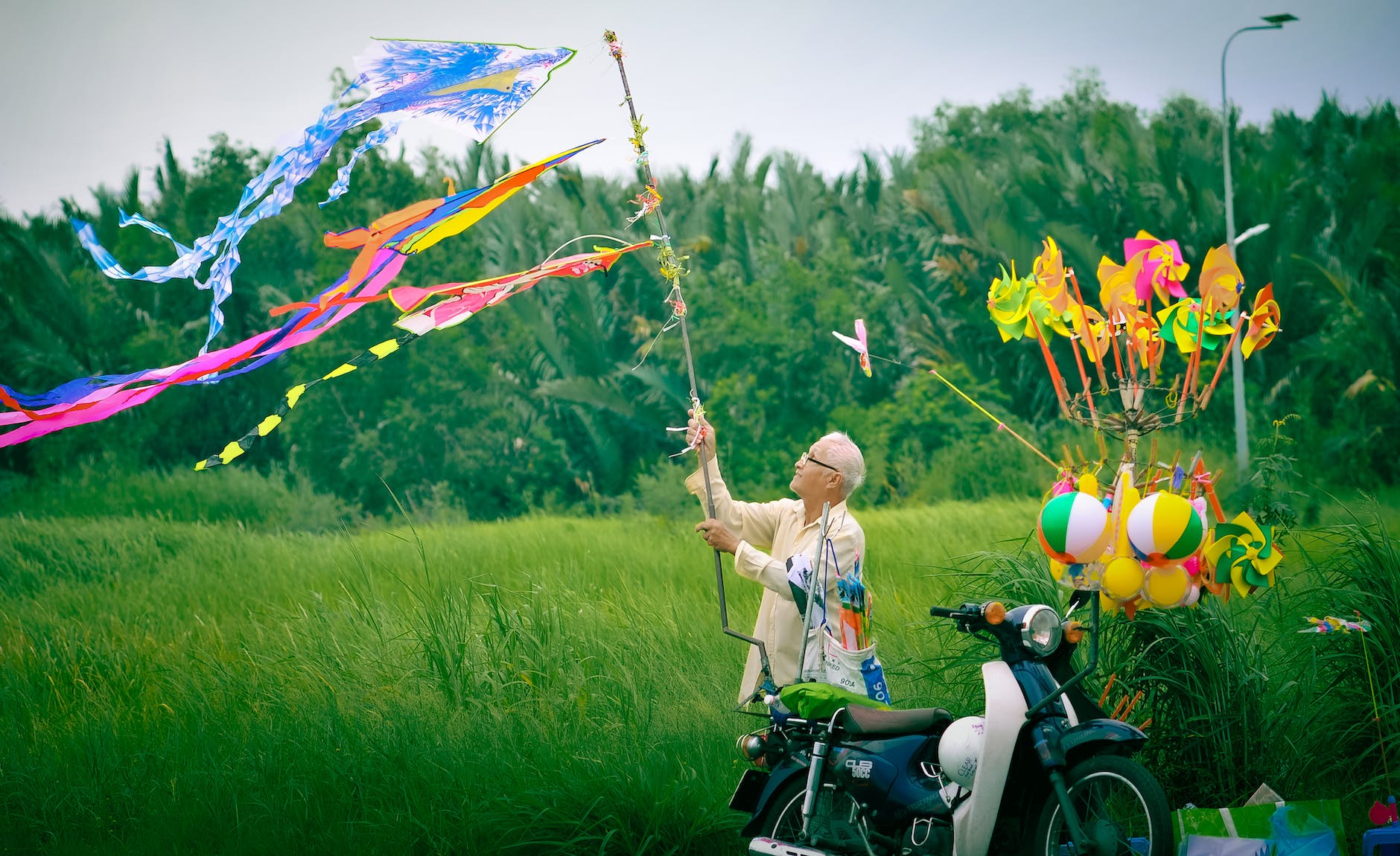man holding stick with kites on wind by motor scooter